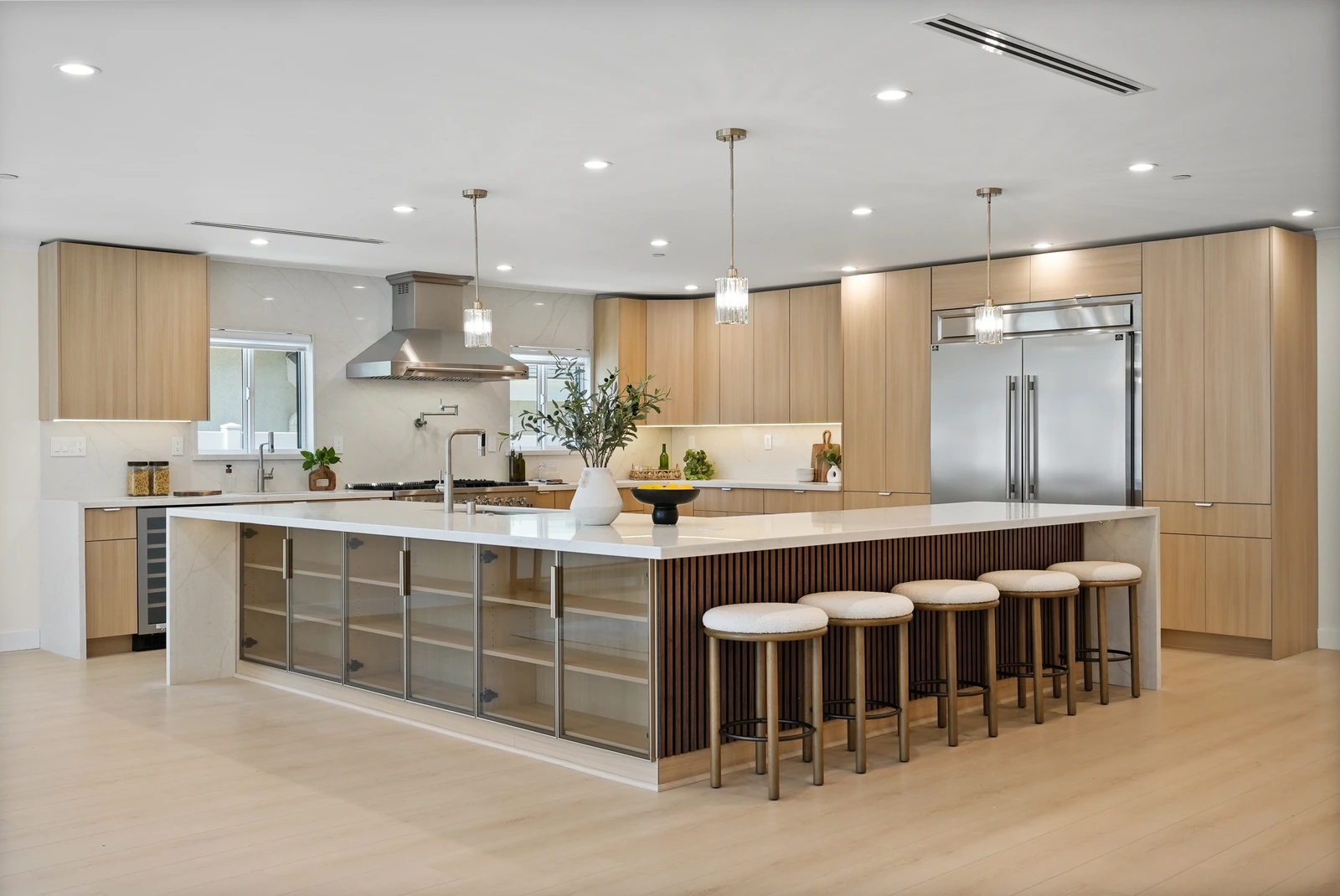 Modern kitchen with light wood cabinetry, a white waterfall island, pendant lights, and pale wood floors