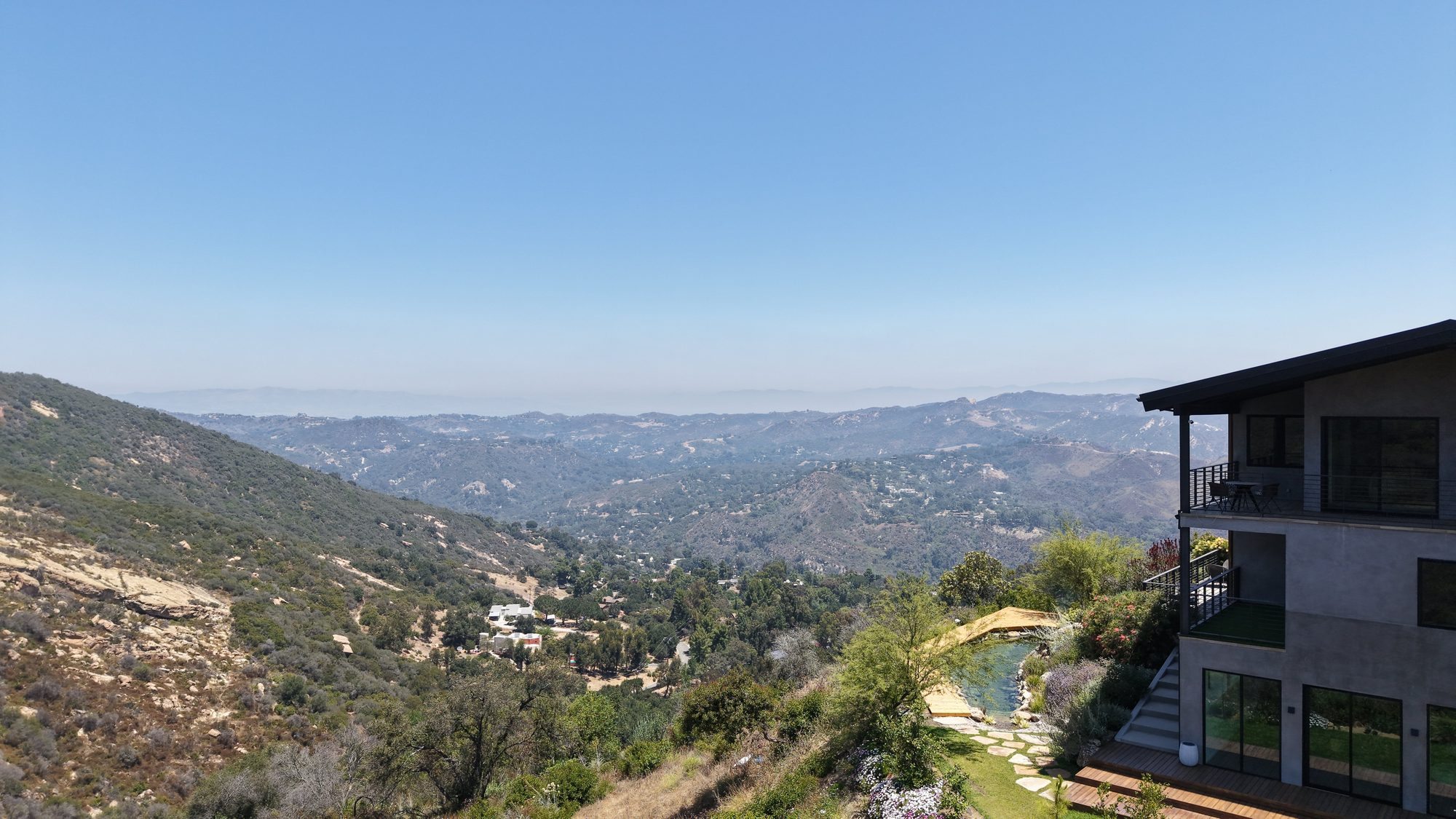 Aerial view of a modern hillside home with a natural pool overlooking canyon ranges