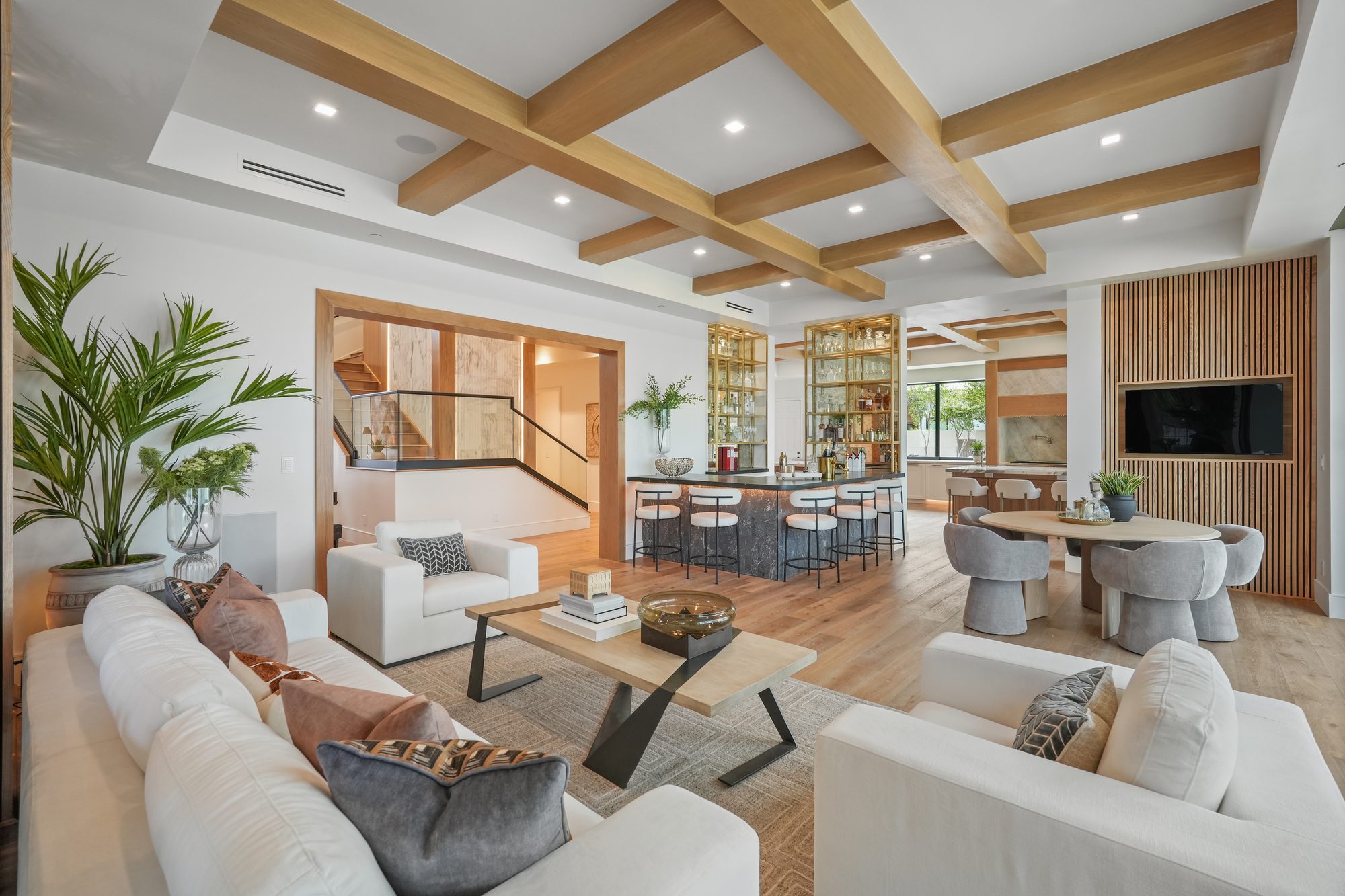 Open great room with white oak beamed ceiling, brass display shelving and marble bar