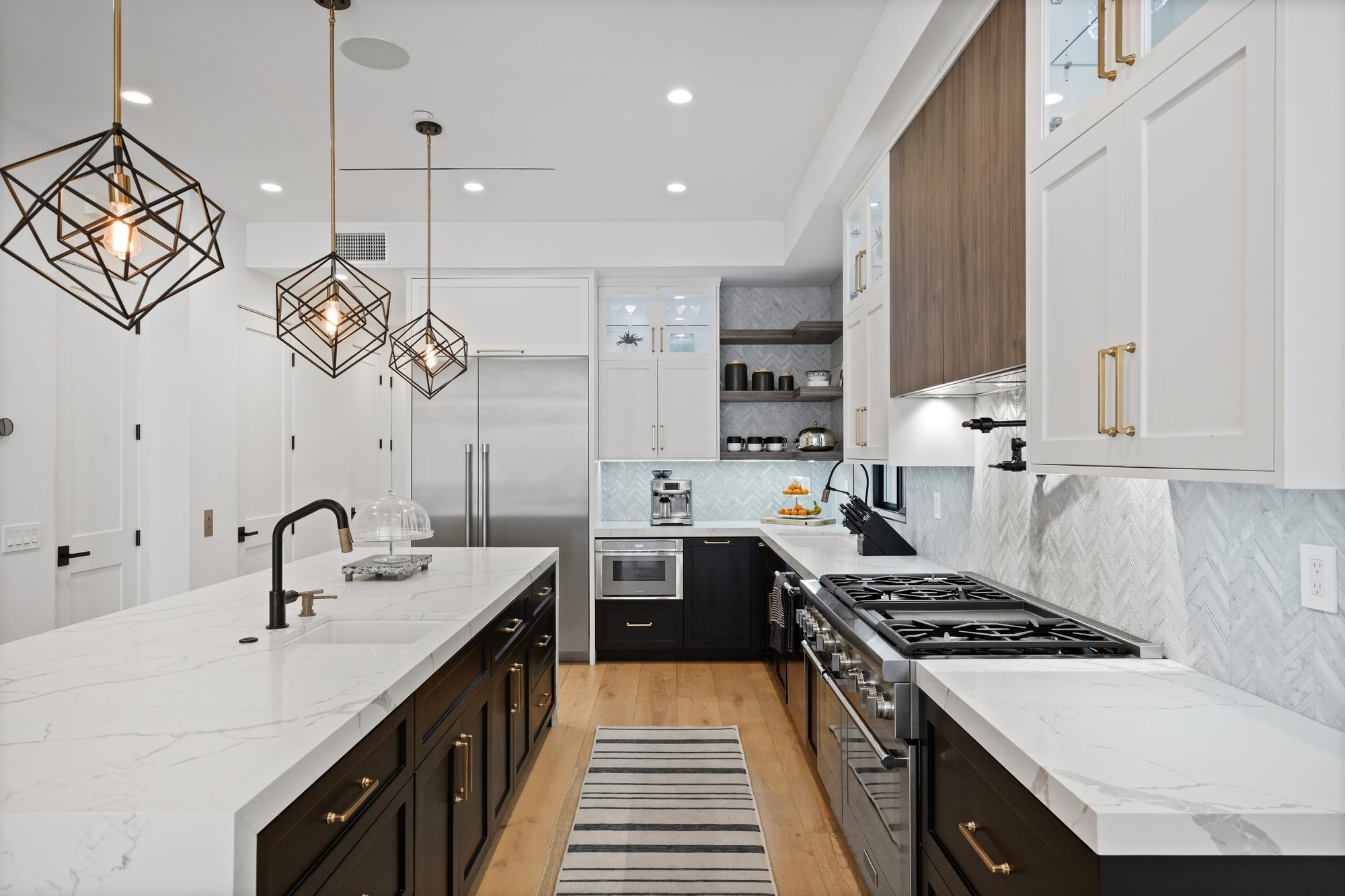Kitchen with waterfall marble island, geometric brass pendants and professional range