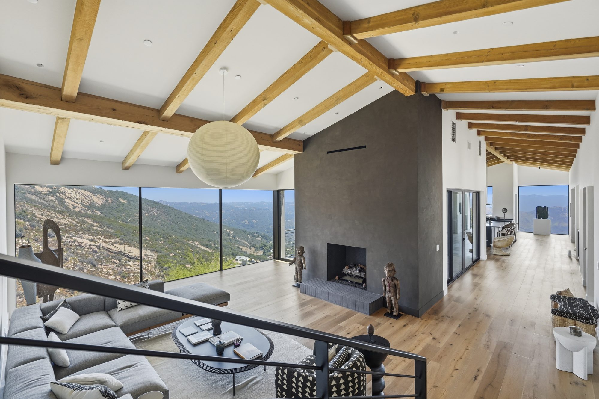 Living room with exposed wood beams, sculptural fireplace and floor-to-ceiling canyon views