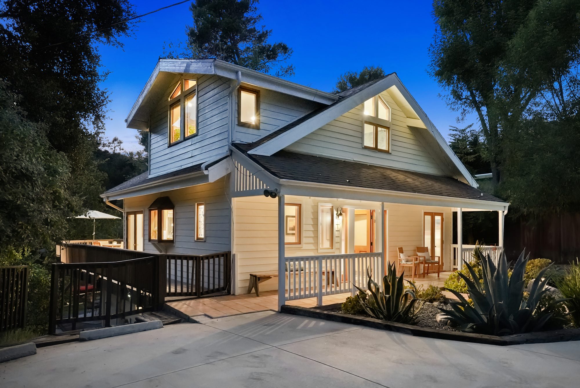 Two-story craftsman home at twilight with warm interior lights and wraparound porch